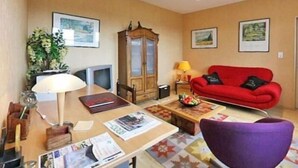 Ein Wohnzimmer mit einem roten Sofa, einem violetten Sessel, einer Holzkommode, einem Tisch mit Zeitschriften und einer Lampe.