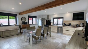 Een moderne keuken met een eethoek, met een groot schiereiland, houten balken en uitzicht op de omgeving.