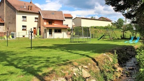 Een woonwijk met huizen, een trampoline, een schommel en een kleine beek.