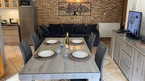 Een eetgedeelte met een houten tafel voor vier personen, een bank en een televisie op de achtergrond.