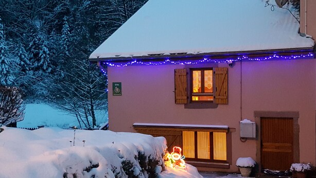 Een gebouw met een met sneeuw bedekte dak, een verlichte kerstboom, en een bord waarop 'Gîte' staat.