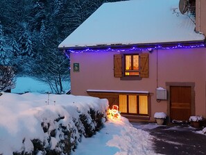 Un edificio con techo nevado, un árbol de Navidad iluminado y un letrero que dice 'Gîte'.