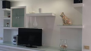 A modern living room with a flat-screen TV, a glass coffee table, and a decorative cat statue.