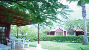 A covered outdoor seating area with white plastic chairs and a table, surrounded by well-maintained grass and palm trees.