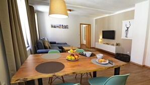 Un soggiorno moderno con un tavolo da pranzo in legno, sedie color petrolio, un divano e una televisione montata a parete.