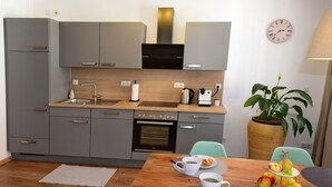 Una cucina compatta con mobili grigi, forno integrato, macchina da caffè e zona pranzo con tavolo in legno apparecchiato per la colazione.