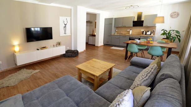 Un soggiorno moderno con un divano grigio, un tavolino in legno e una TV a parete.
