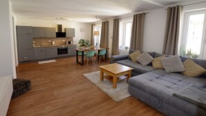 Un appartamento moderno con un divano grigio, un tavolino da caffè in legno e un angolo cottura con pensili grigi e un tavolo da pranzo.