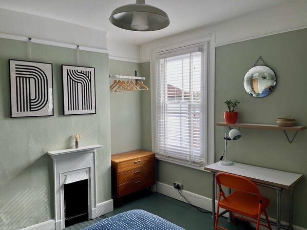 A room with a fireplace, a desk, an orange chair, a mirror, and abstract wall art. - Lilly Cottage - Fisherman's Cottage Whitstable (Whitstable)