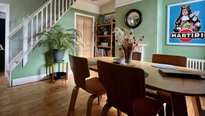 A dining area with a wooden table, chairs, a potted plant, and a bookshelf. - Lilly Cottage - Fisherman's Cottage Whitstable (Whitstable)