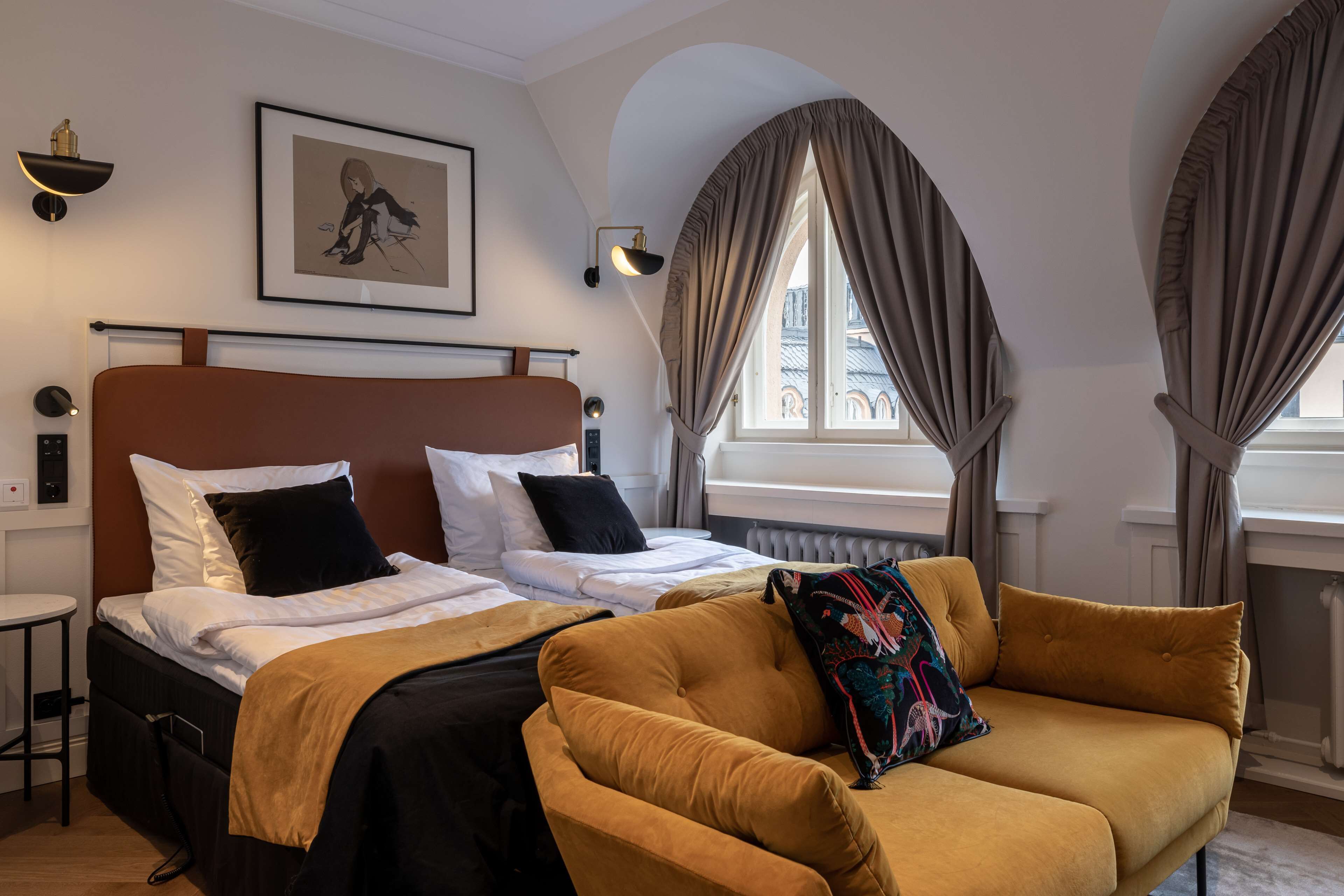 A hotel room with two beds, a sofa, a framed picture on the wall, and a window with curtains.