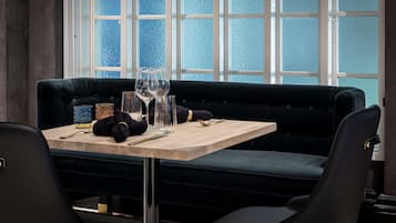 Un comedor con una mesa de madera, un banco tapizado azul oscuro y vistas a través de un gran ventanal con vidrio azulado.