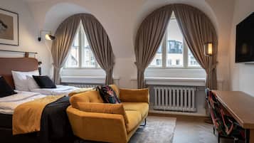 A hotel room with a bed, a sofa, a desk, and two windows with curtains.