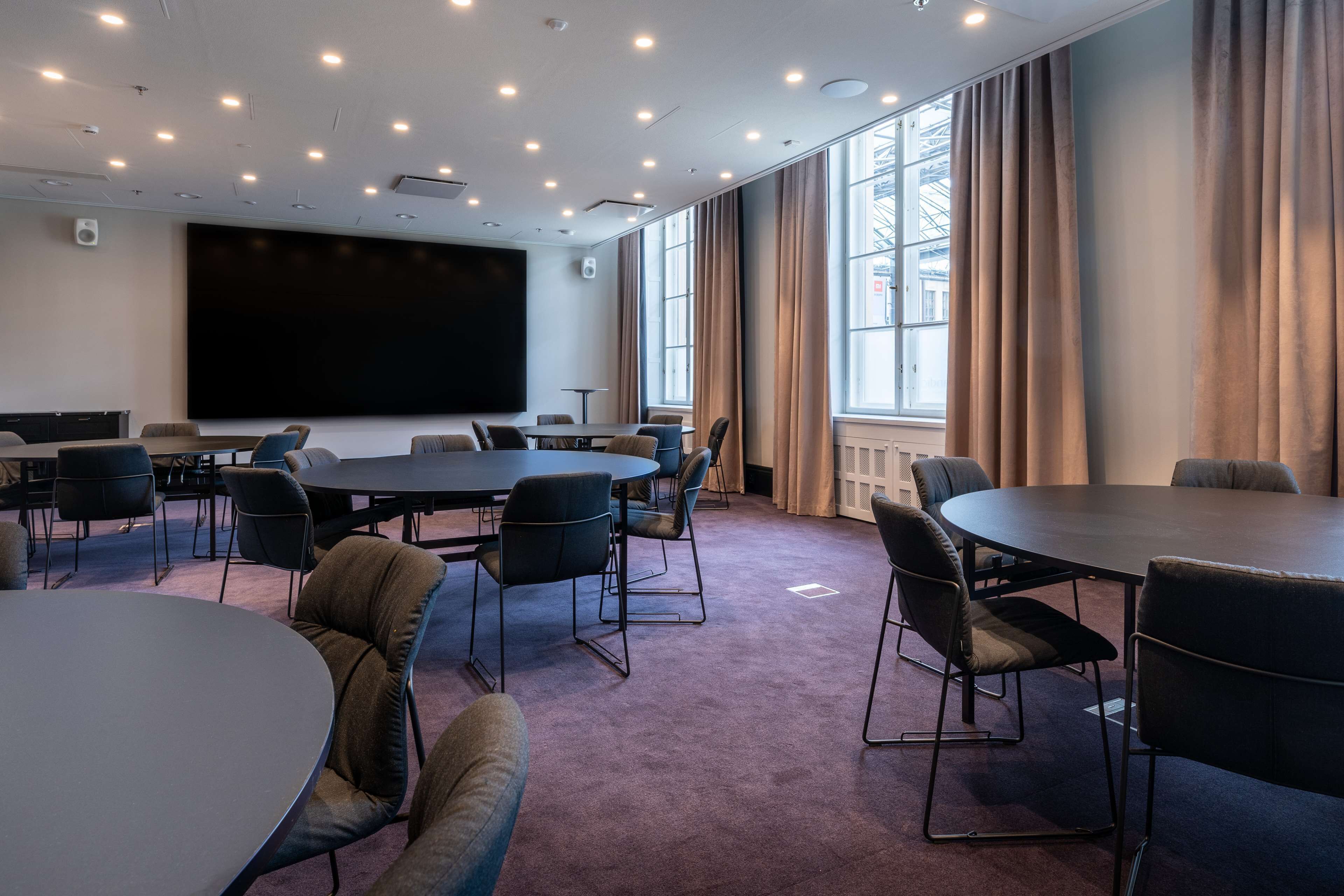 Un salón de conferencias con una pantalla grande, varias mesas y sillas.