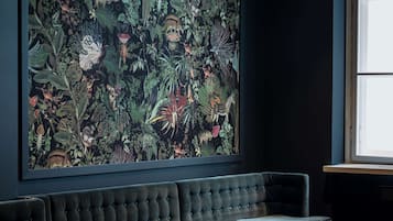 Una habitación con un amplio mural botánico en la pared, un sofá de color oscuro y una ventana con luz natural.