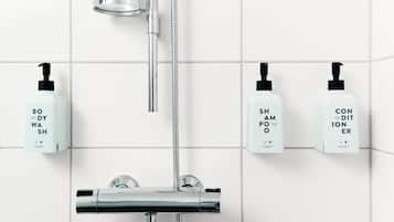 Un baño moderno con cabezal de ducha de cromo, ducha de mano y tres botellas de gel de baño, champú y acondicionador en la pared.