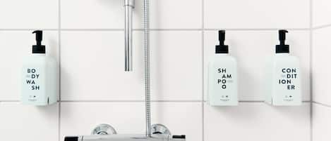 Un baño moderno con cabezal de ducha de cromo, ducha de mano y tres botellas de gel de baño, champú y acondicionador en la pared.