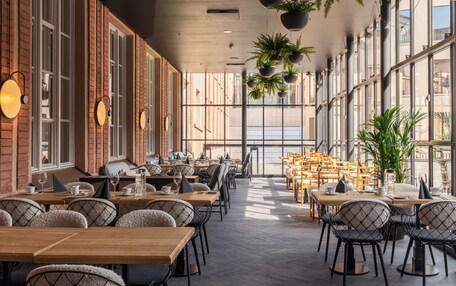 A spacious indoor dining area with brick walls, large windows, and modern furniture.