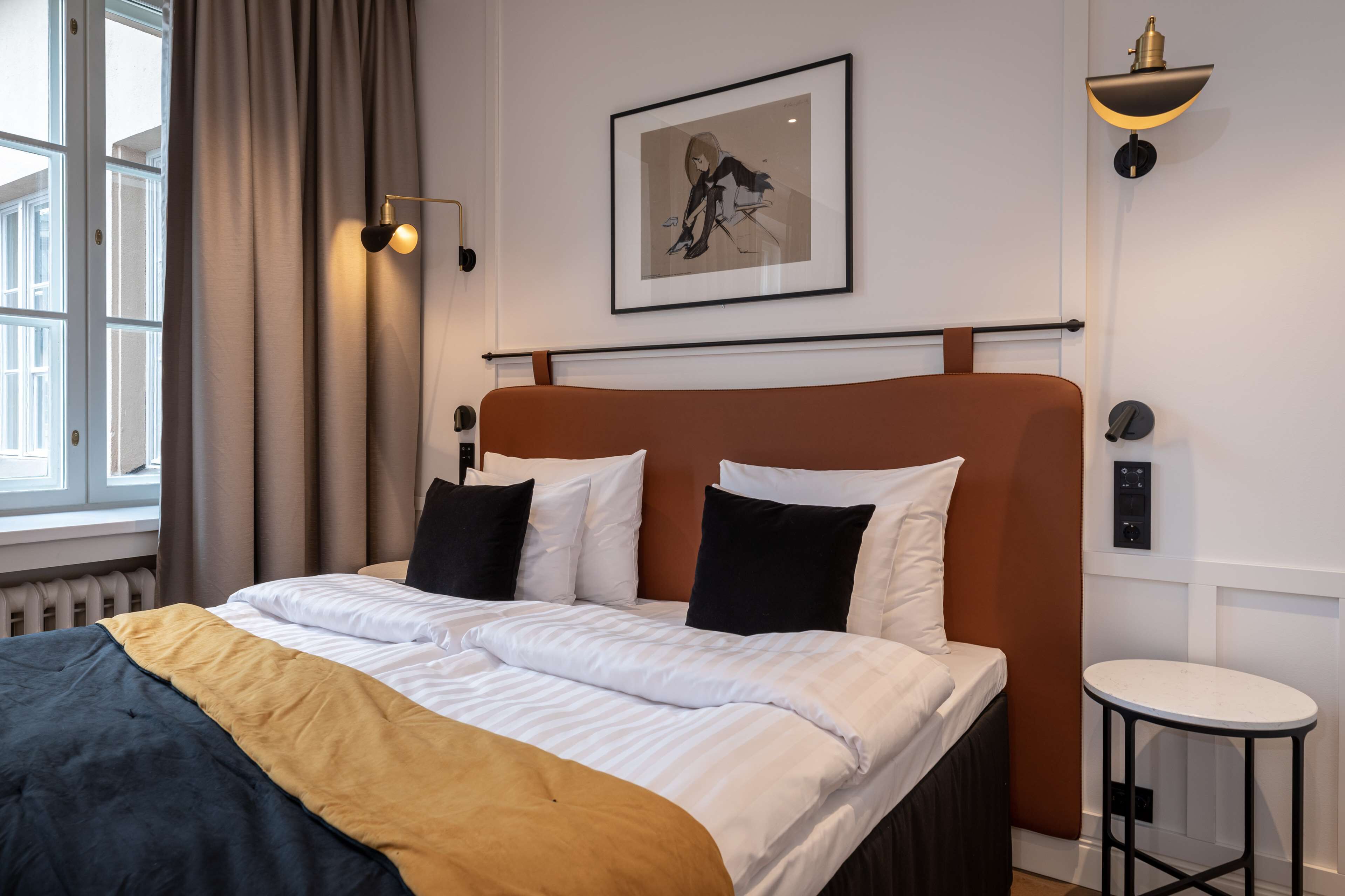 A neatly made bed with white and black pillows, a brown headboard, and a framed picture above it.