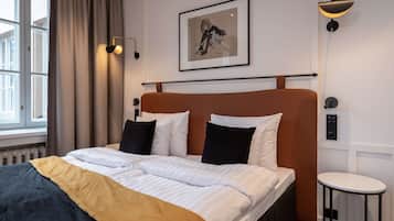 A neatly made bed with white and black pillows, a brown headboard, and a framed picture above it.