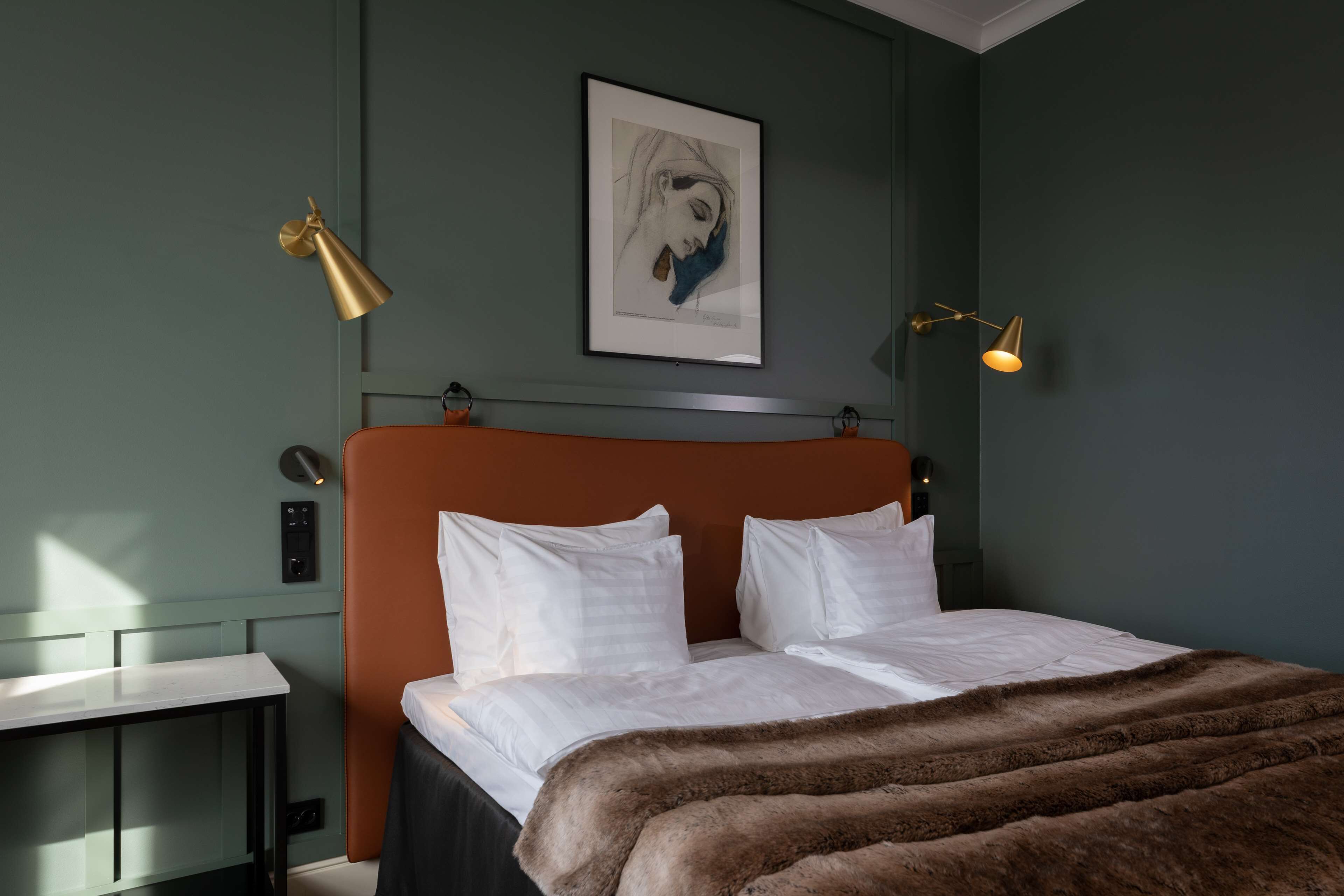 Un dormitorio moderno con una cama grande, dos mesitas de noche, una obra de arte enmarcada en la pared y dos lámparas fijadas a la pared.