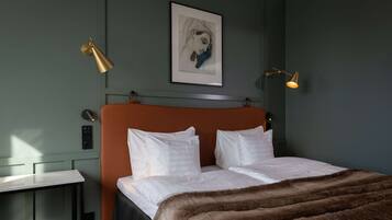 Un dormitorio moderno con una cama grande, dos mesitas de noche, una obra de arte enmarcada en la pared y dos lámparas fijadas a la pared.
