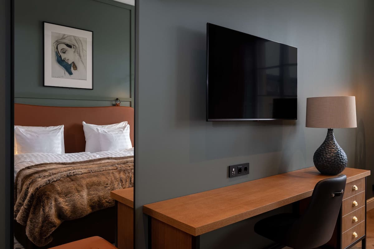 A hotel room with a bed, a desk, a television, and a lamp.