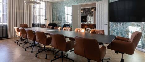 A conference room with a long table, brown leather chairs, and a large screen.
