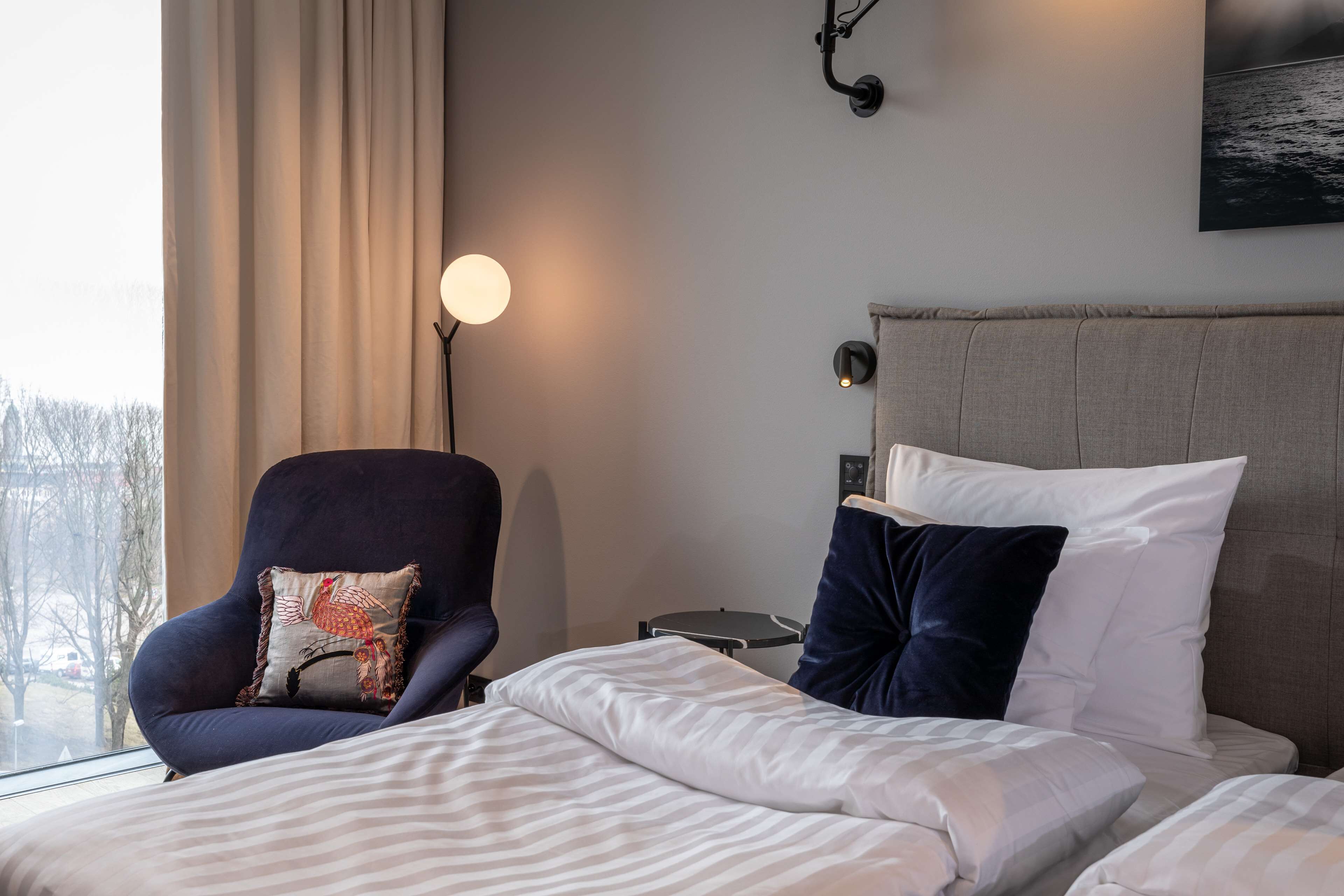 Ett hotellrum med en säng, en stol, ett nattduksbord och en lampa.