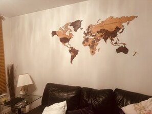 Ett vardagsrum med en världskarta på väggen, en lädersoffa, ett soffbord i glas och en lampa.