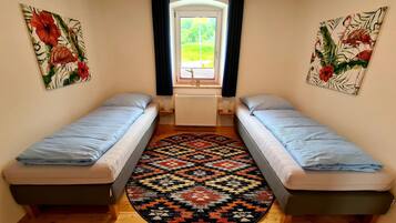 Una stanza modesta con due letti singoli, un tappeto decorato e due elementi decorativi floreali alle pareti.
