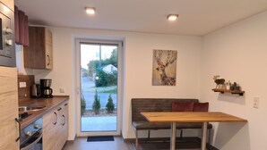A modern kitchen with a built-in oven, a coffee maker, and a sink. There is a sliding glass door leading to a patio with a view of a road and greenery. - Modern vacation apartment "wohnung-nummer-1" in rural area near Regensburg (Pielenhofen)