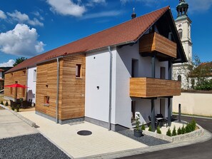 A modern building with a wooden facade, a balcony, and a clock tower in the background.