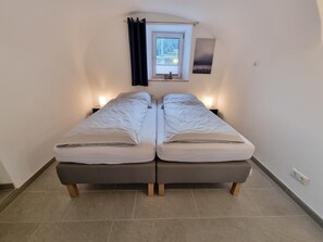 Habitación con dos camas individuales, una ventana, una mesita de noche y un cuadro en la pared.
