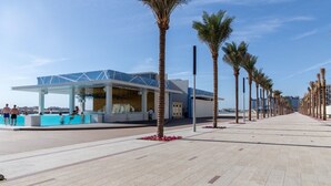 Ein modernes Gebäude mit Glasfassade, einem Poolbereich und einem von Palmen gesäumten Weg.