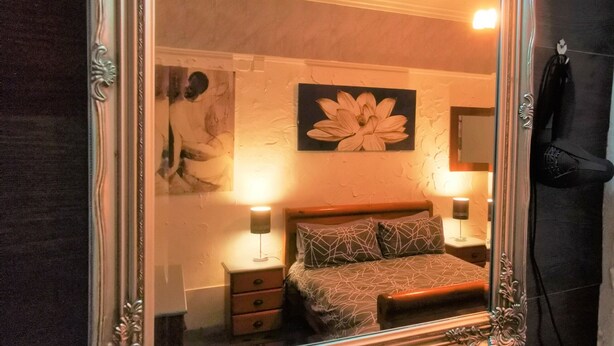 A mirror with an ornate frame reflecting a bedroom with a bed, nightstands, and wall art. - Immaculate 1-bed Apartment in Blackpool - Sleeps 5 (Blackpool)