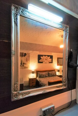 A mirror with an ornate frame reflecting a bedroom with a bed, nightstands, and wall art. - Immaculate 1-bed Apartment in Blackpool - Sleeps 5 (Blackpool)