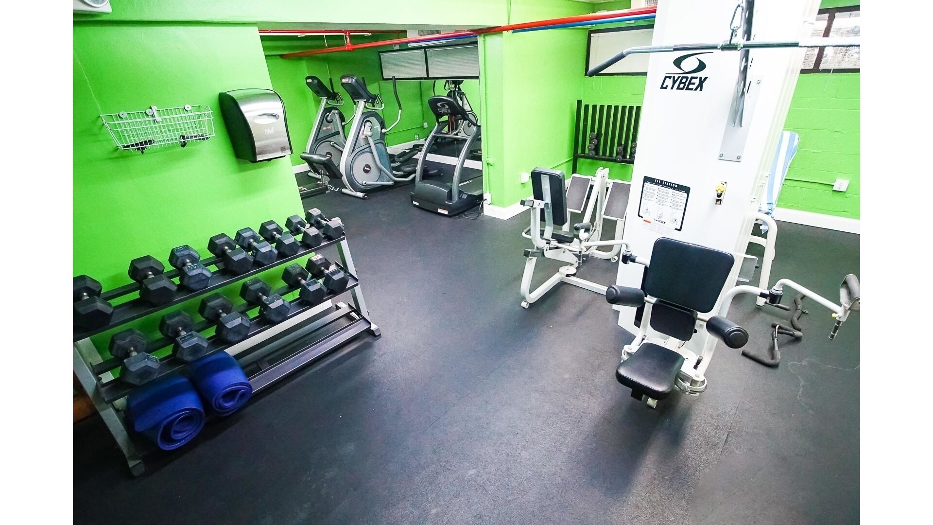 A gym with green walls, exercise equipment, dumbbells, and a Cybex machine.