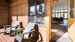 Eine Holzhütte mit zwei Adirondack-Stühlen auf der Veranda, einem Essbereich mit Tisch und Stühlen und großen Fenstern, die einen Blick auf die umliegende Landschaft bieten.