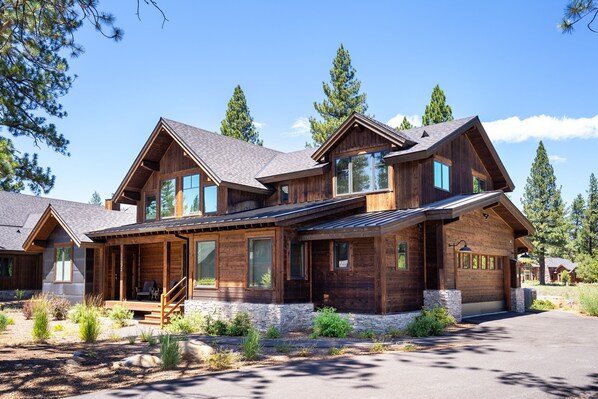 Une grande maison en bois à plusieurs étages, avec des fondations en pierre, de grandes fenêtres et un porche couvert.