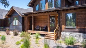 Eine zweistöckige Blockhütte mit Steinunterbau, großen Fenstern und einer Veranda mit Sitzgelegenheit im Freien.