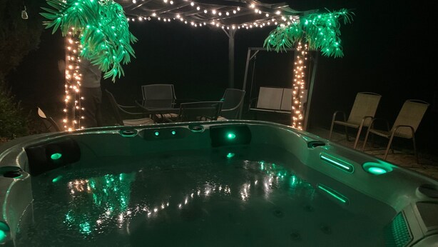 Ein Whirlpool im Freien mit grüner Beleuchtung, umgeben von Stühlen und einer Lichterkette.