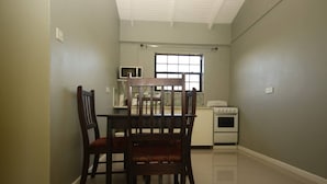 A small kitchen with a dining table and chairs, a window, and a stove. - Veronica's - Breathe Easy - Reduit Apartment #1 (Rodney Bay)
