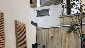 Une terrasse extérieure moderne avec un revêtement de sol en bois, un coin salon jaune doté de coussins et une clôture en bois.