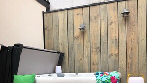 Une terrasse en bois avec un matelas et des coussins, une lanterne et un objet blanc posé sur une table en bois.