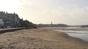 Une plage bordée d’une promenade où s’alignent des bâtiments, d’une jetée et, au loin, du clocher d’une église.