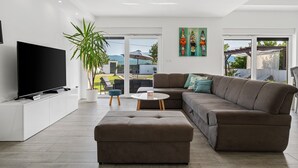 A modern living room with a large flat-screen TV, a sectional sofa, a coffee table, and a potted plant.