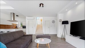A modern living room with a grey sofa, a white coffee table, and a TV on a white stand.