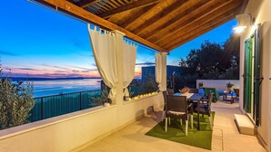 A covered outdoor patio with a view of the sea, wooden beams, a table with chairs, and a green door. - Seaview Villa Lemaro, a 2-bedroom villa with a 28 sqm private pool in Krilo Jesenice (Jesenice)