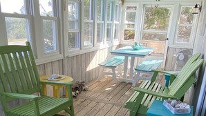 A covered porch with wooden flooring, green and yellow chairs, and a table. - Salvo Sandbox: Ocean-Side, Dog-Friendly Cottage (Salvo)